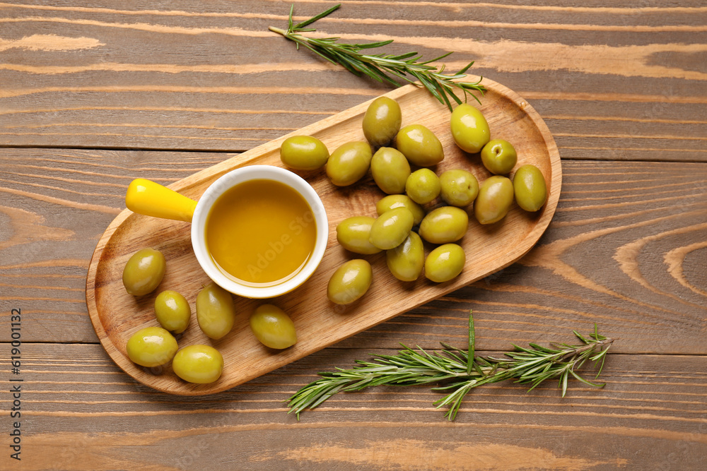 Ripe olives and bowl with oil on wooden background