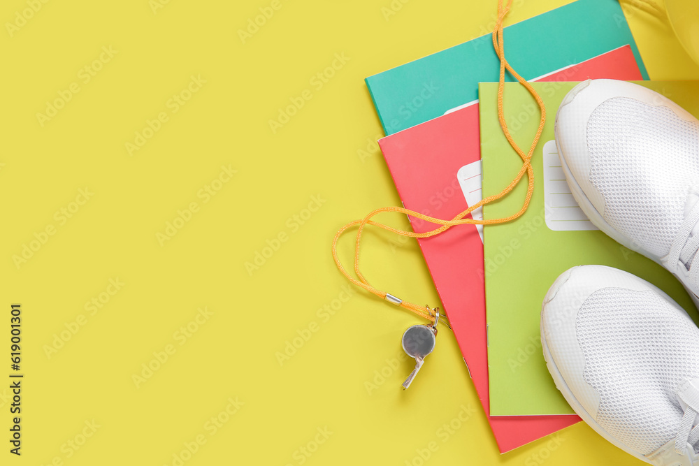 Sneakers with whistle and notebooks on yellow background