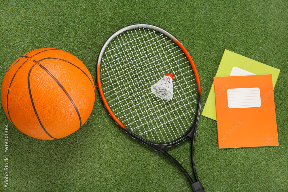 Badminton shuttlecock with racket, ball and notebooks on color background