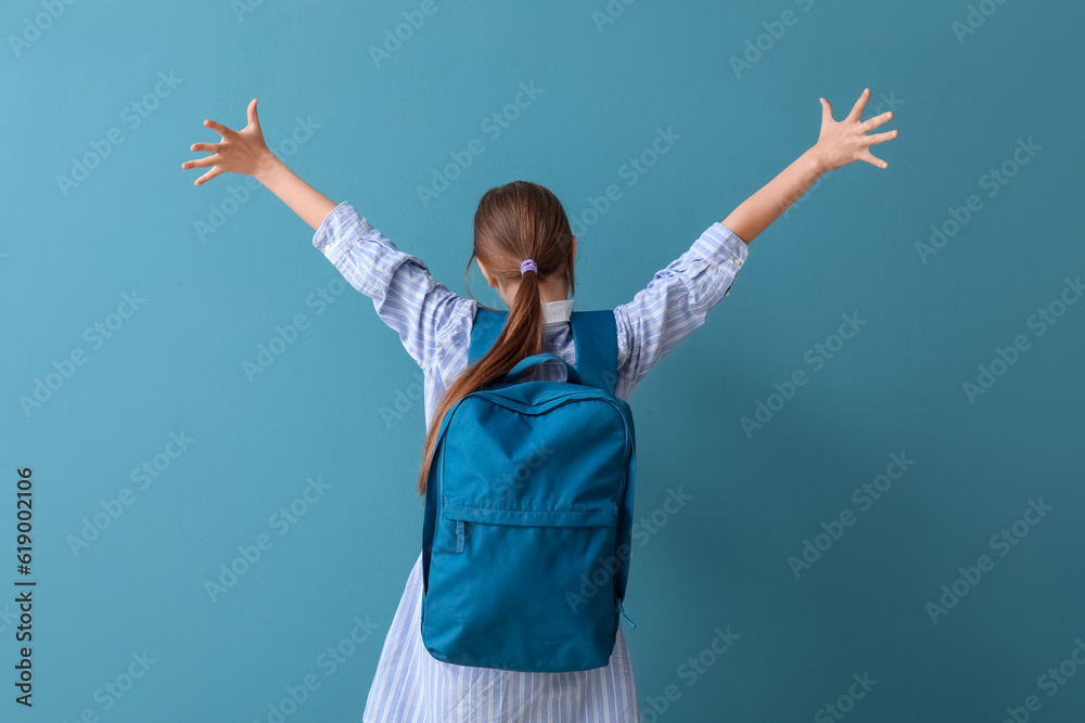 Little schoolgirl with backpack on blue background, back view