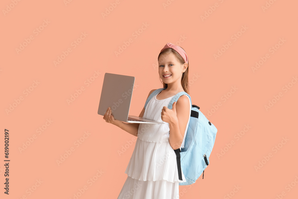 Little schoolgirl with laptop and backpack showing thumb-up on pink background