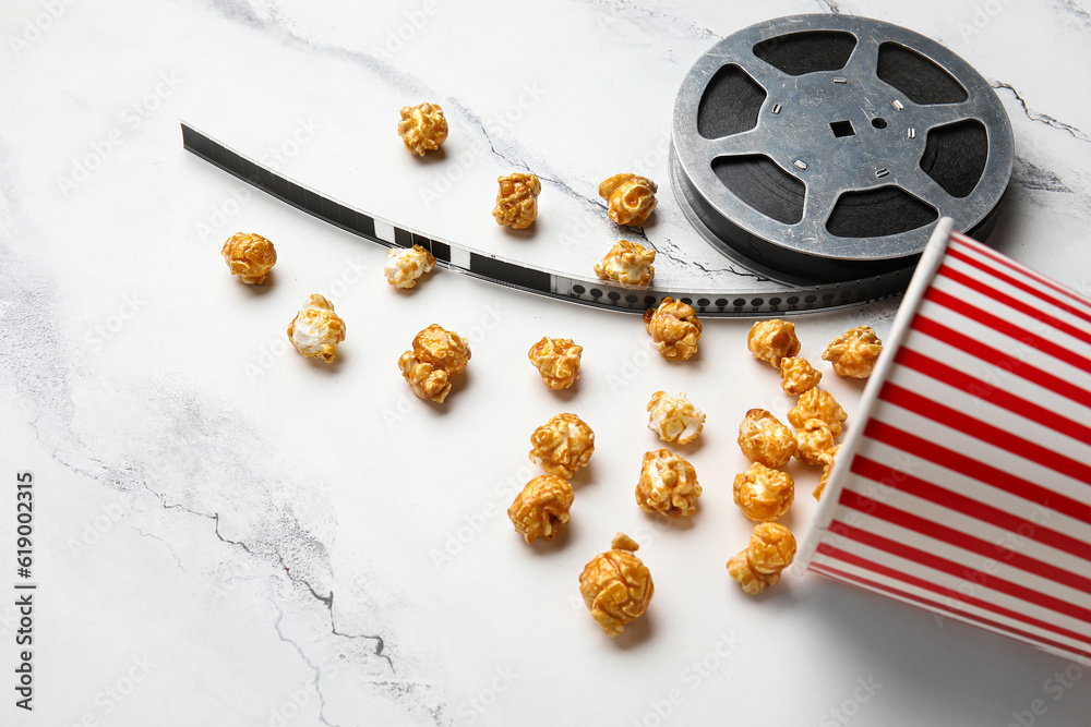 Bucket with tasty popcorn and film reel on white background