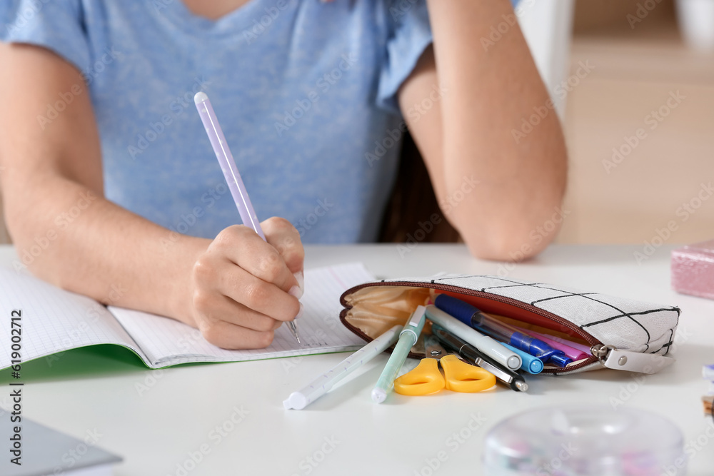 Little girl with pencil case writing at table, closeup