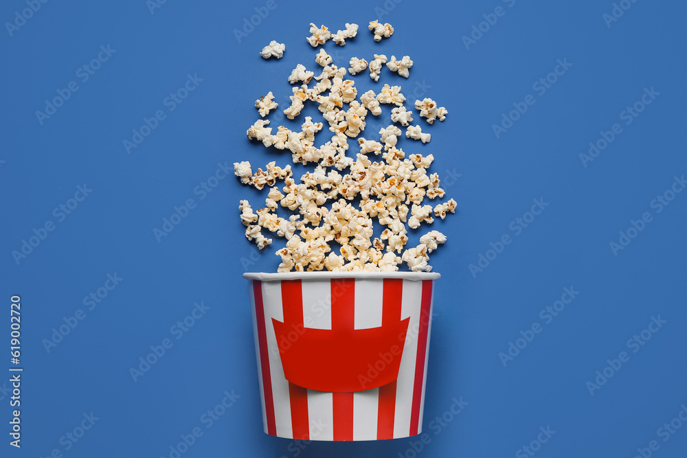 Bucket with tasty popcorn on blue background