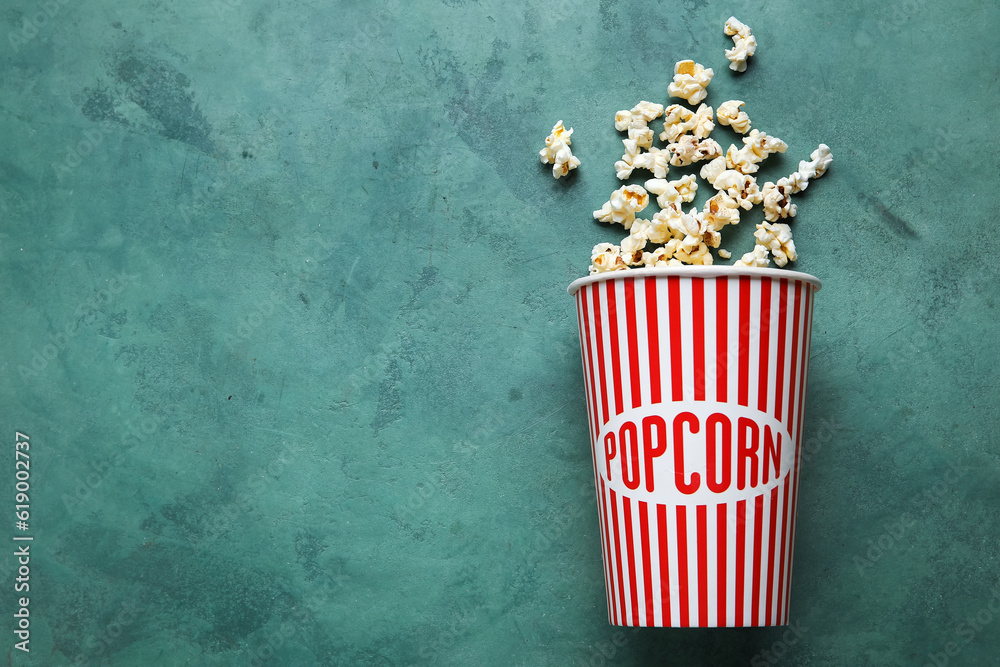 Bucket with tasty popcorn on green background