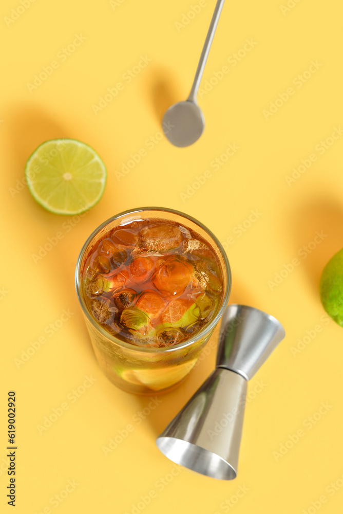 Glass of cold Cuba Libre cocktail on yellow background