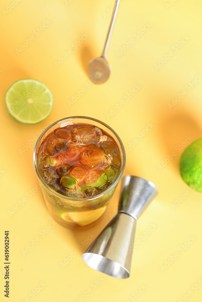 Glass of cold Cuba Libre cocktail on yellow background