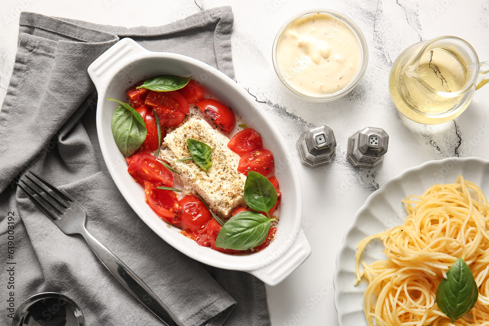 Baking dish with tasty tomatoes, feta cheese and pasta on white marble background