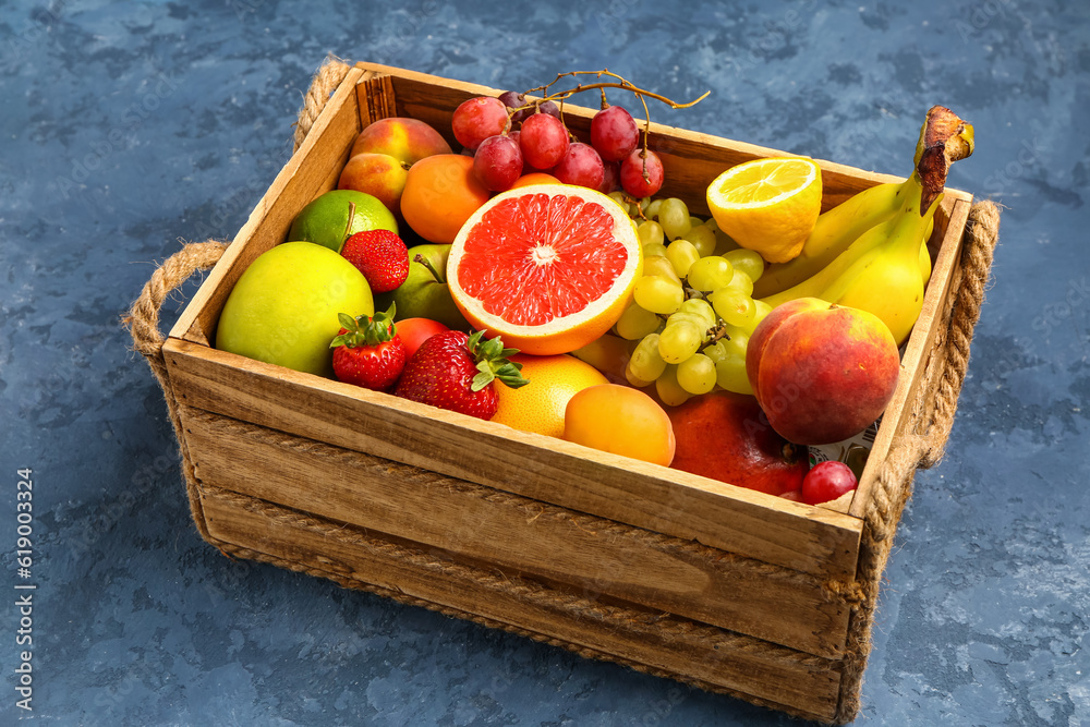 Wooden box with different fresh fruits on blue background