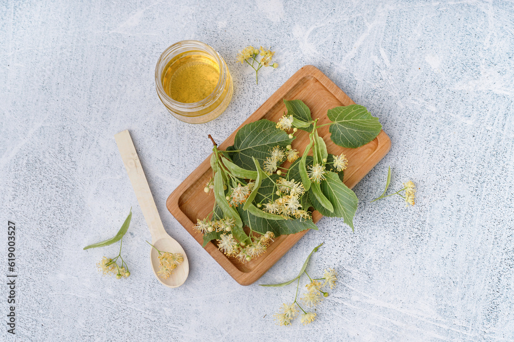 Wooden board with fresh linden flowers and honey on light background