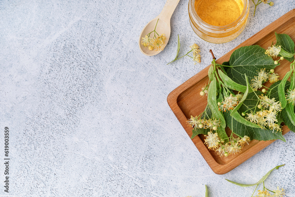 Wooden board with fresh linden flowers and honey on light background