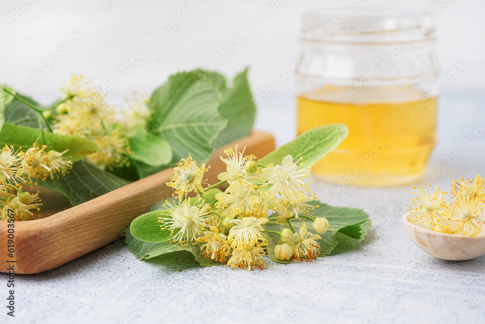 Wooden board with fresh linden flowers and honey on light background, closeup