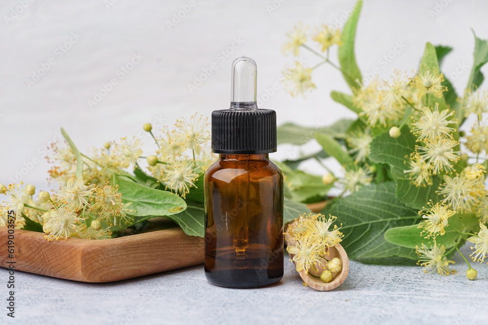 Bottle of essential oil and aromatic linden flowers on light background