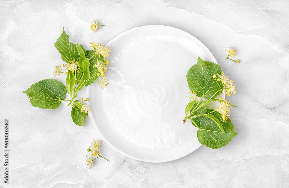 Plate and aromatic linden flowers on light background