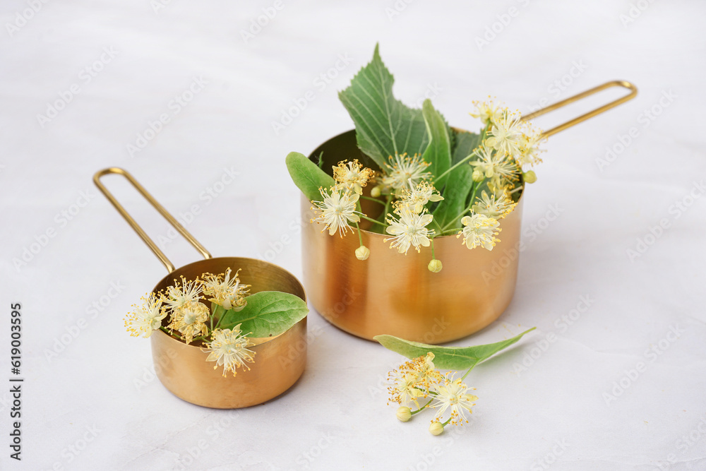 Golden saucepans with aromatic linden flowers on light background