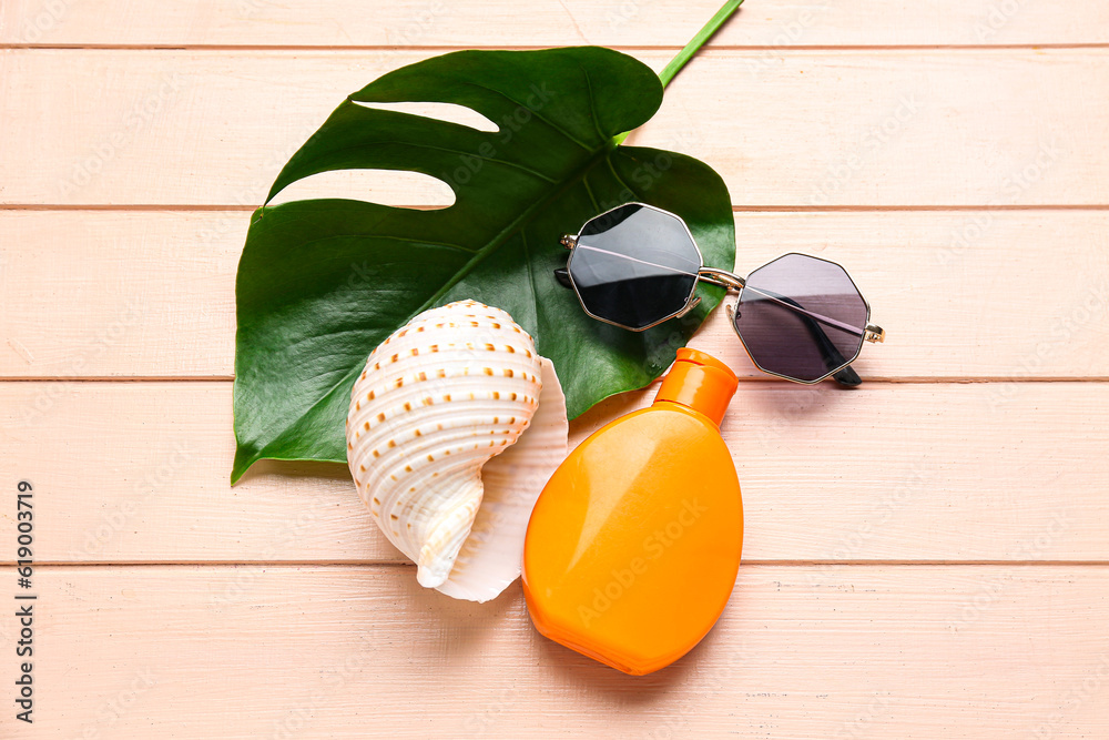 Sunglasses with palm leaf, seashell and bottle of sunscreen cream on pink wooden background