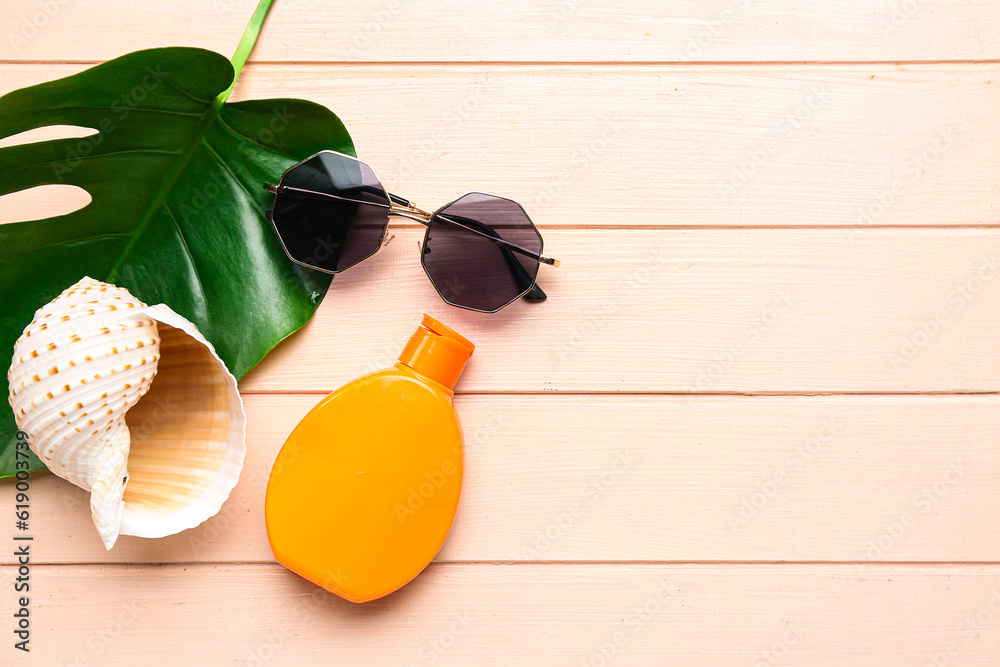 Sunglasses with palm leaf, seashell and bottle of sunscreen cream on pink wooden background