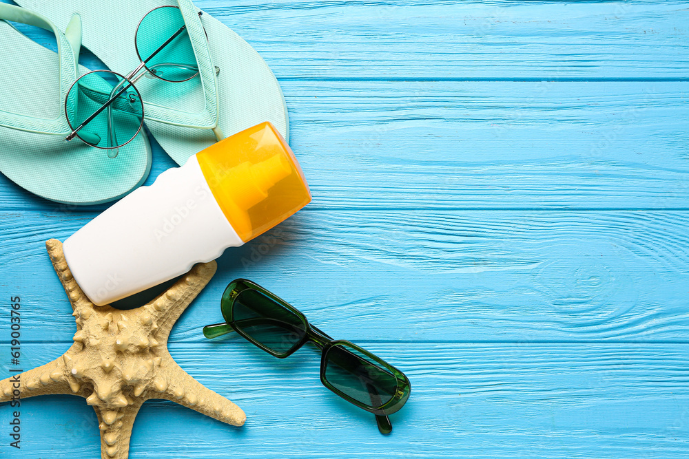 Flip flops with sunglasses, starfish and bottle of sunscreen cream on blue wooden background