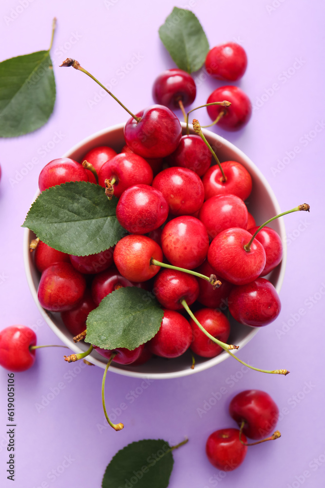 Bowl with sweet cherries and leaves on lilac background