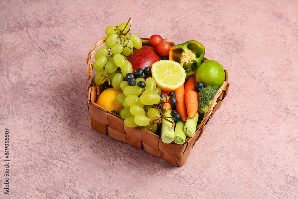 Wicker basket with different fresh fruits and vegetables on pink background