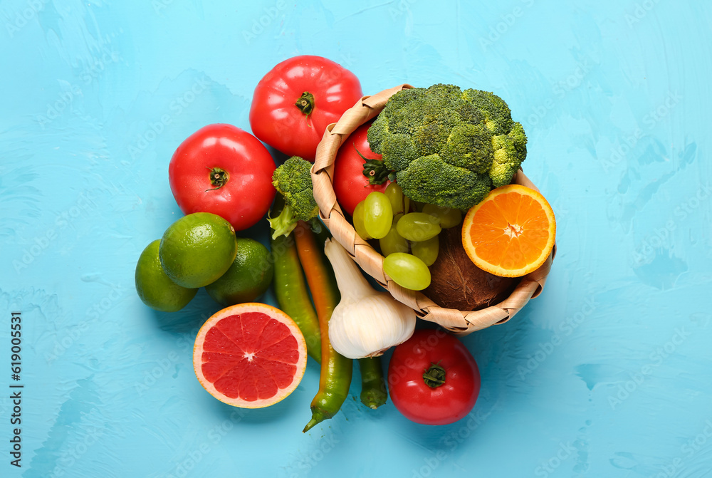 Wicker basket with different fresh fruits and vegetables on blue background