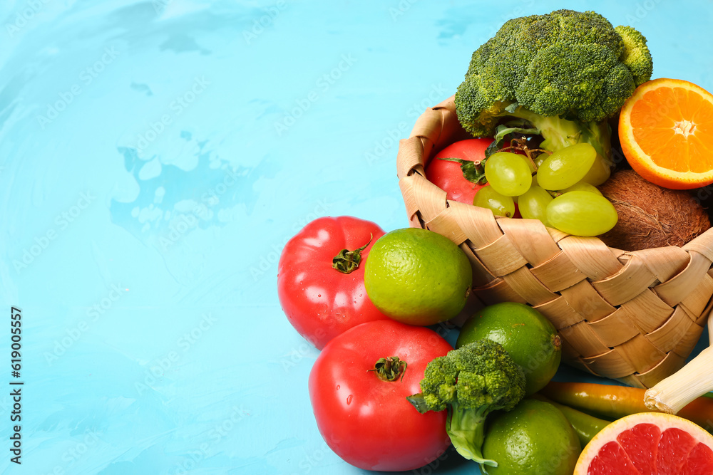 Wicker basket with different fresh fruits and vegetables on blue background, closeup