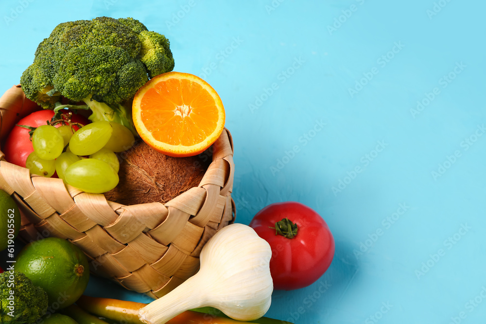 Wicker basket with different fresh fruits and vegetables on blue background, closeup