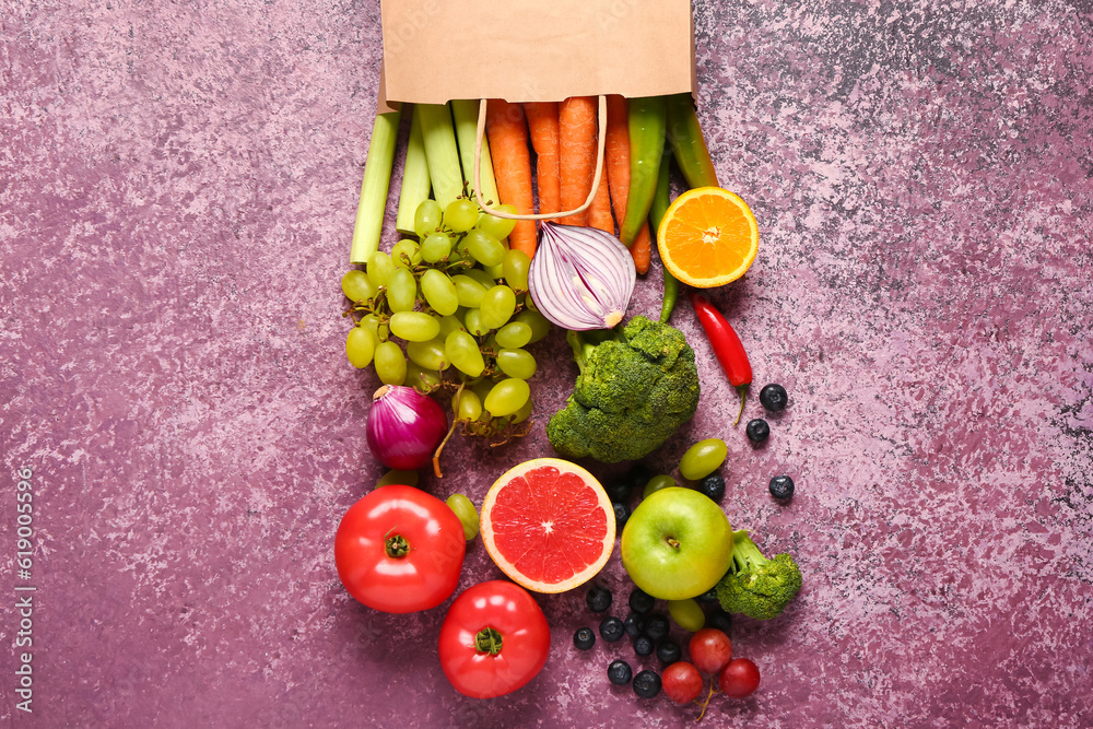 Paper bag with different fresh fruits and vegetables on purple background