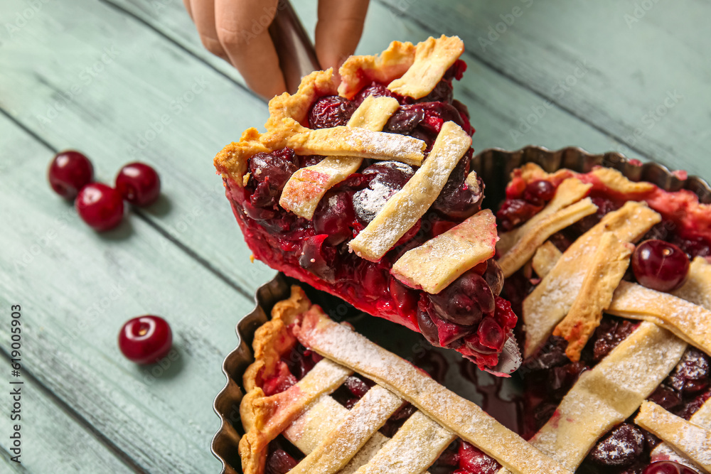 Woman taking piece of tasty cherry pie on blue wooden table