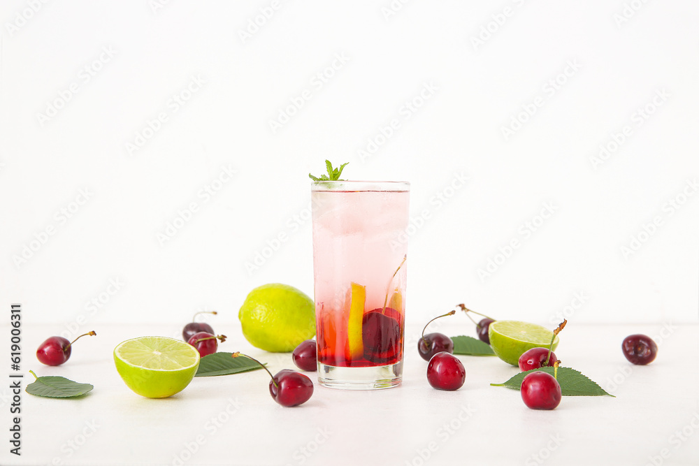 Glass of tasty cherry lemonade with lime and mint on white background