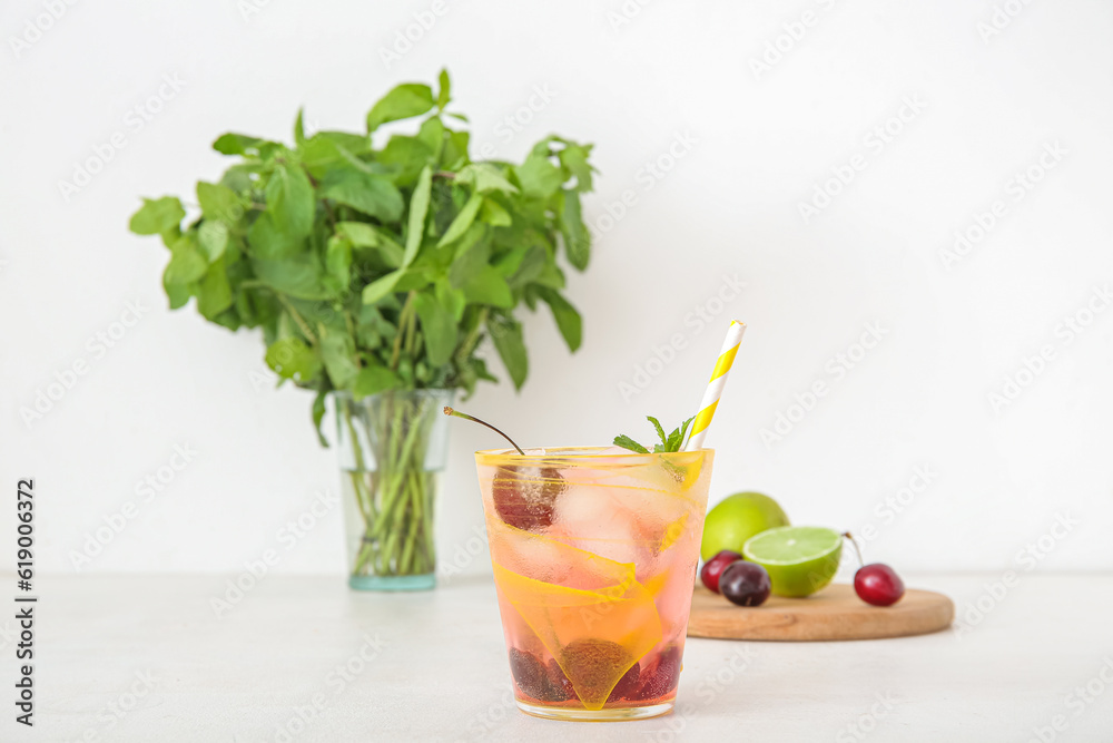 Glass of tasty cherry lemonade, mint and wooden board with limes on white background