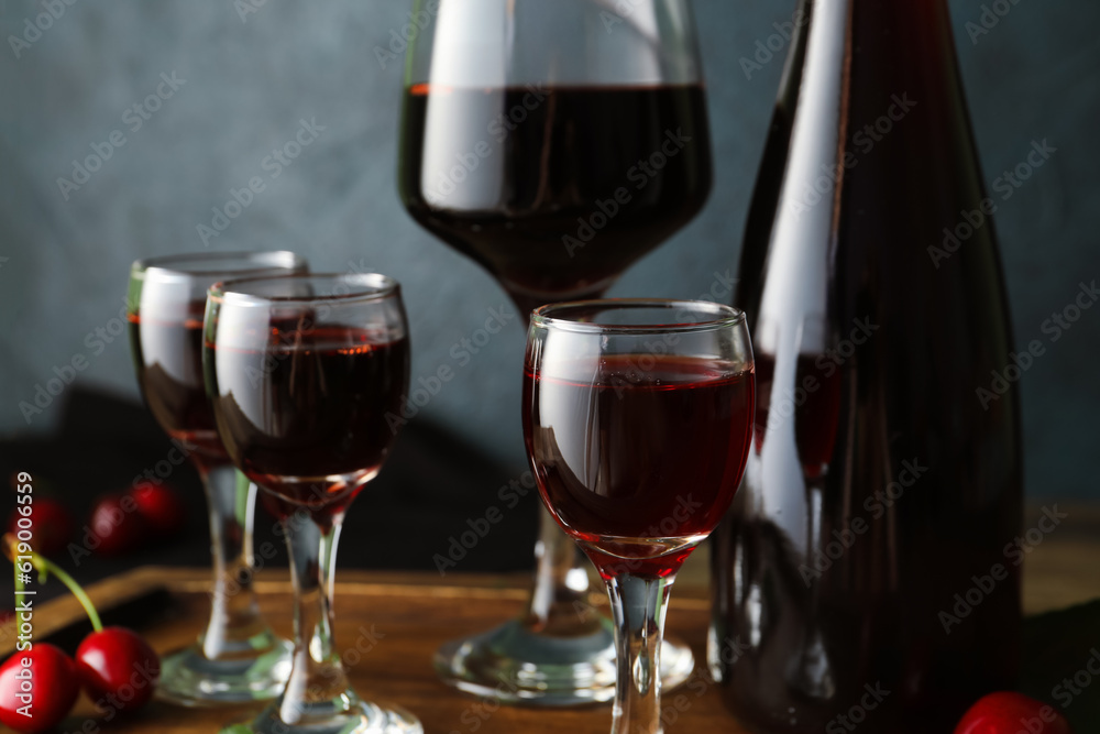 Glasses and bottle with sweet cherry liqueur on dark background, closeup