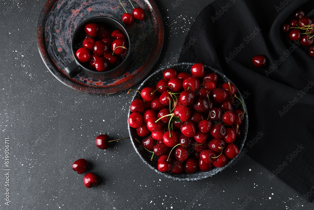 Bowl and cup with sweet cherries on black background