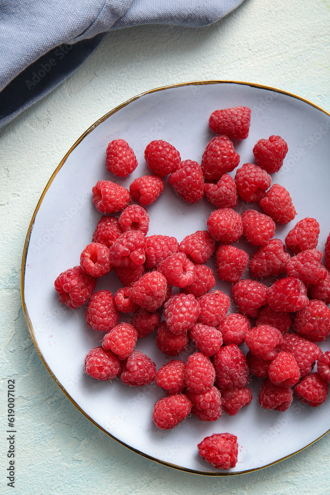 Plate with fresh raspberries on light blue background