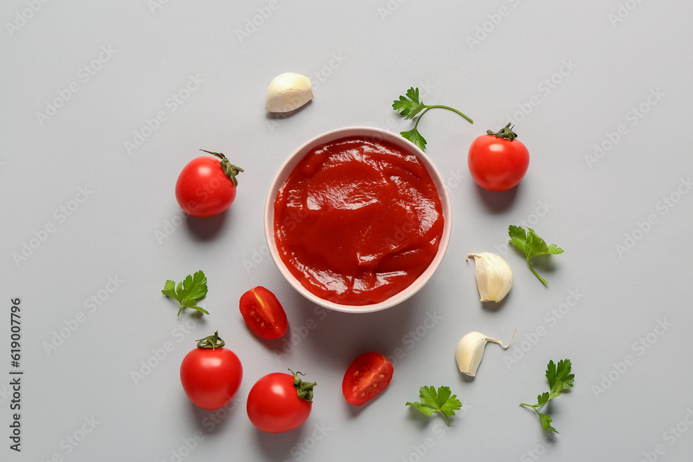 Bowl with tomato paste and fresh vegetables on grey background