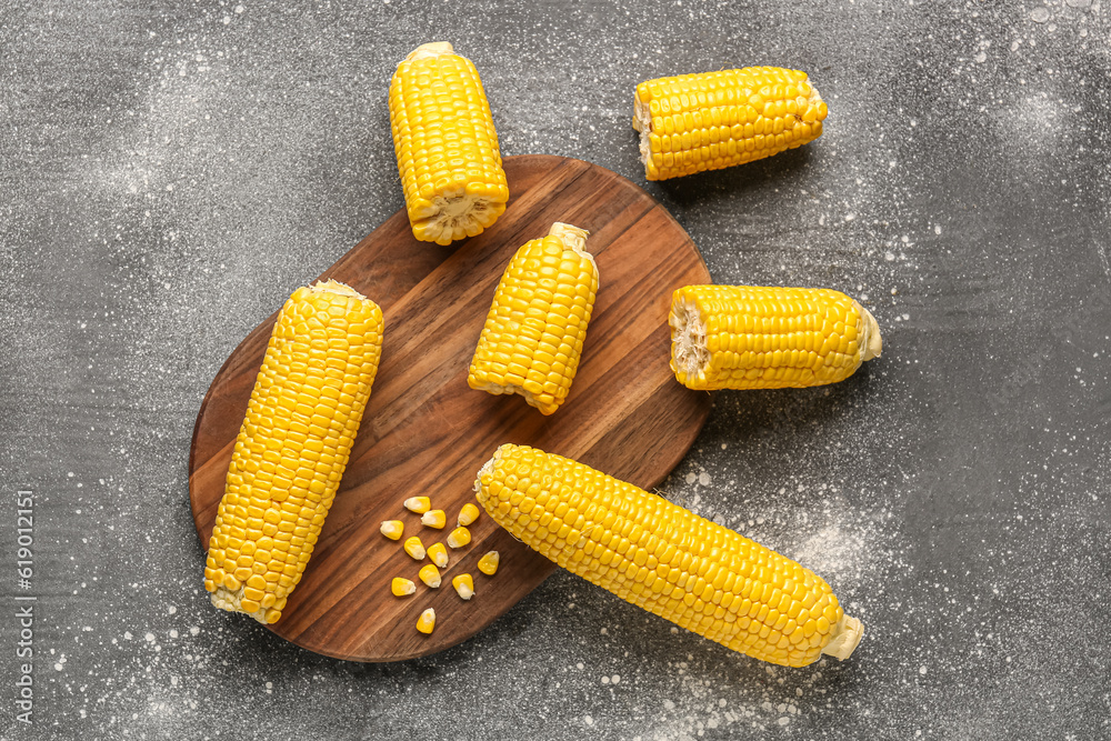 Wooden board with fresh corn cobs on grey background