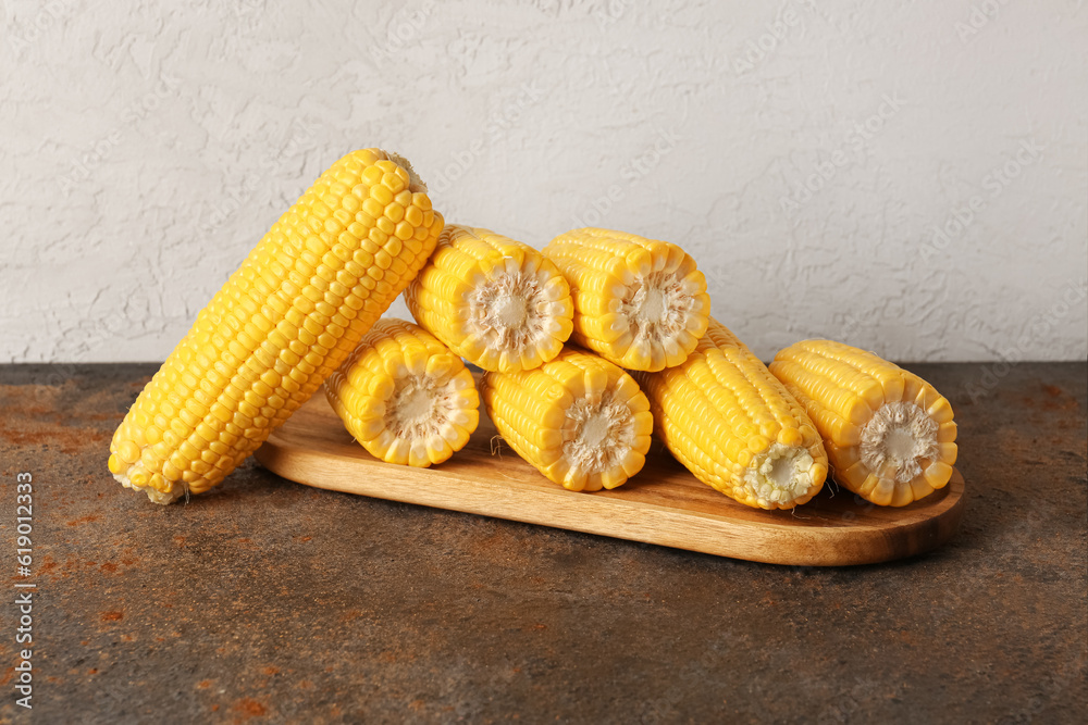 Wooden board with fresh corn cobs on dark table