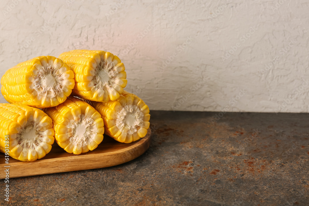 Wooden board with cut fresh corn cobs on dark table