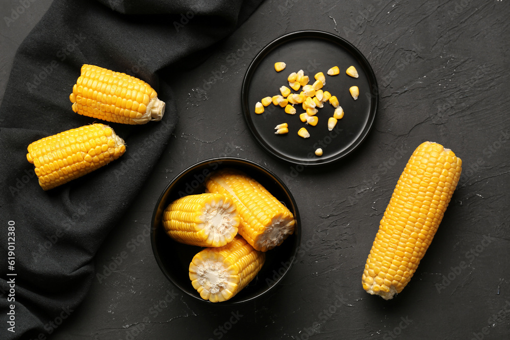 Bowl of fresh corn cobs and plate with seeds on black background