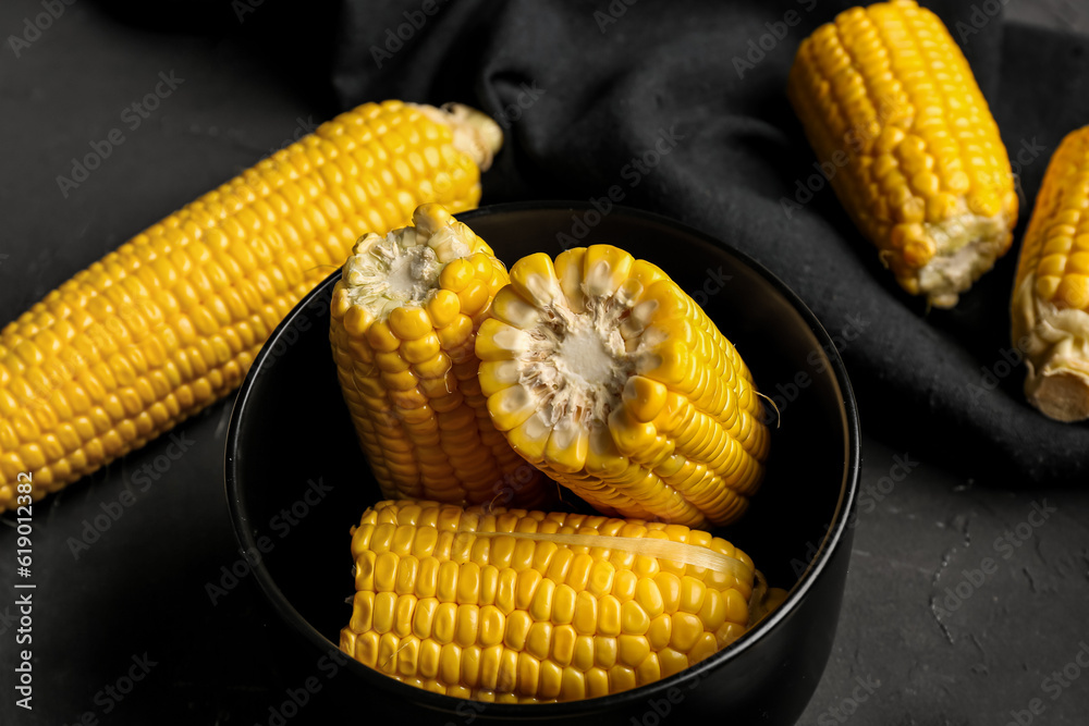 Bowl with cut fresh corn cobs on black background