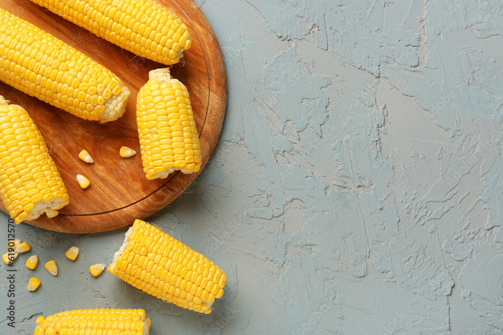 Wooden board with fresh corn cobs and seeds on blue background