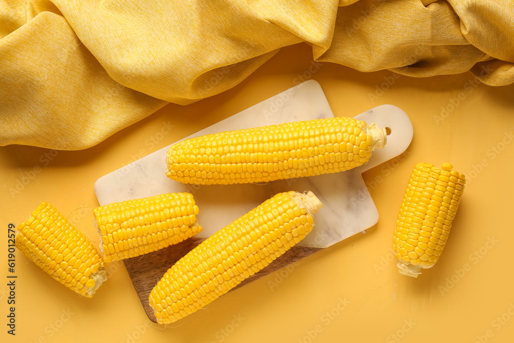 Board with fresh corn cobs on yellow background