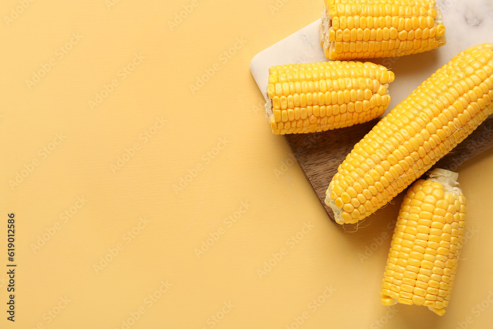 Board with fresh corn cobs on yellow background