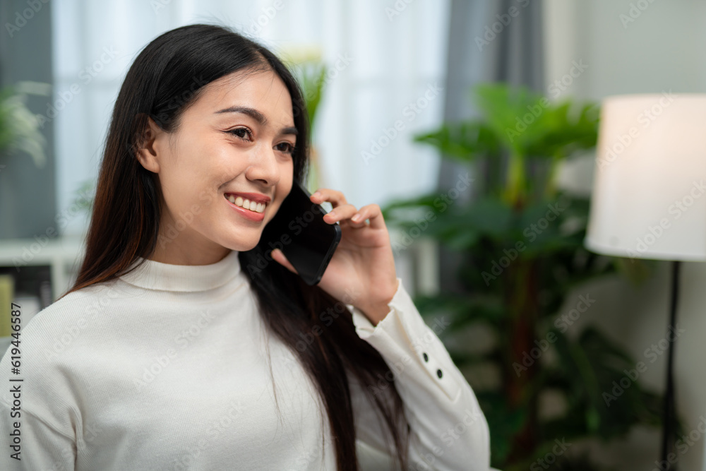 Asian woman smiling while talking on the phone in the living room.