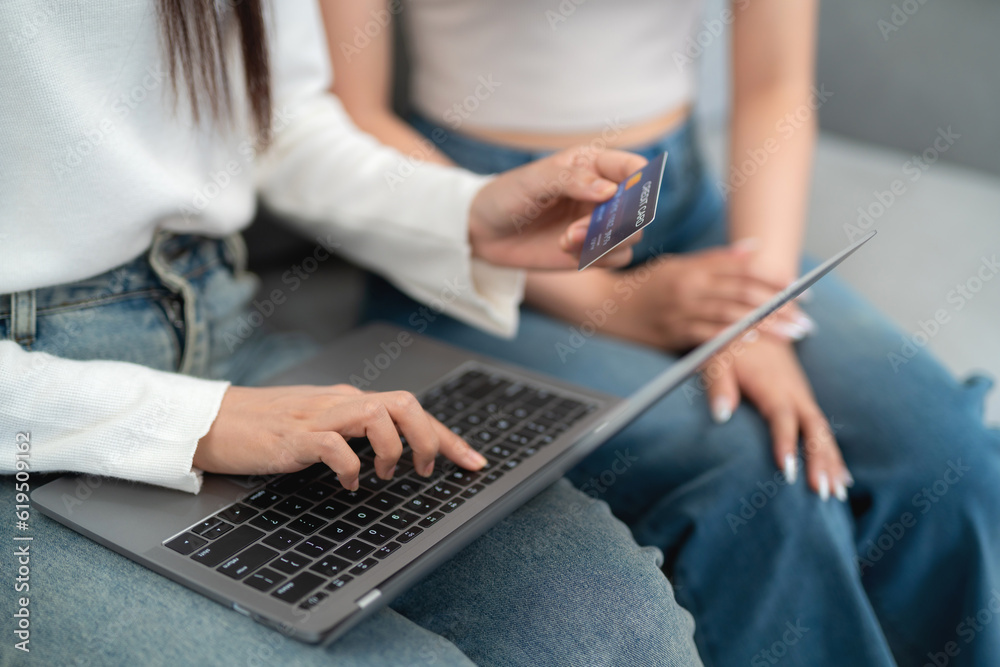 Two asian young women shopping online shopping on laptop with credit card while sitting together on 