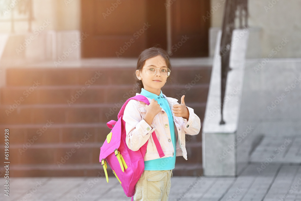 Little girl showing thumb-up outdoors near school