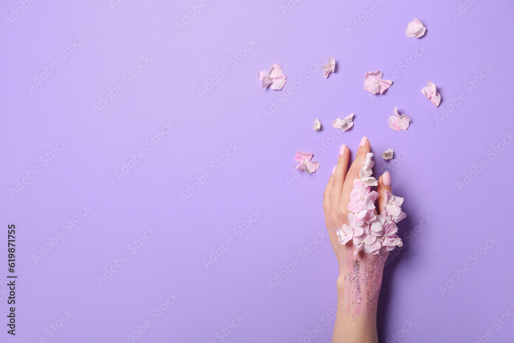 Woman with glitter and floral petals on lilac background. Hand care concept