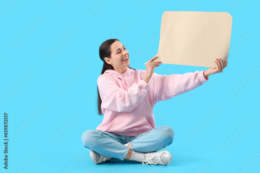 Young woman with blank speech bubble sitting on blue background