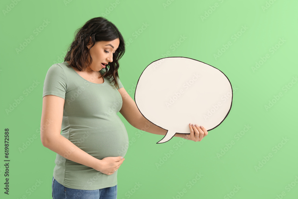 Surprised young pregnant woman with blank speech bubble on green background