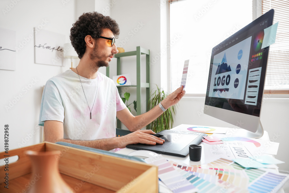 Male graphic designer working with color palette and tablet at table in office